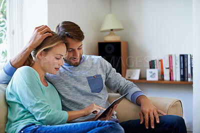 Buy stock photo Shot of a young couple using a digital tablet while relaxing on a sofa at home
