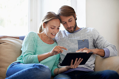 Buy stock photo Shot of a young couple using a digital tablet while relaxing on a sofa at home