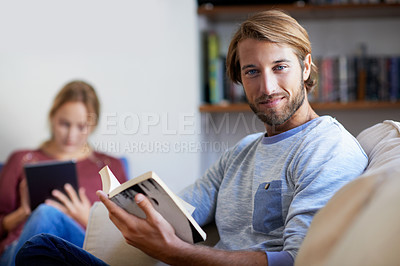 Buy stock photo Portrait of a young man reading a book with his partner in the background