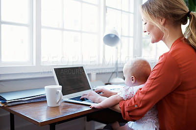 Buy stock photo Shot of a mother using a laptop with her baby sitting on her lap