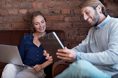 Buy stock photo Shot of a young couple using a digital tablet and laptop while relaxing at home