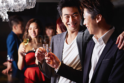 Buy stock photo Shot of two male friends drinking shots together in a club