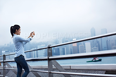 Buy stock photo Shot of a young asian woman taking a picture of the Hong Kong skyline
