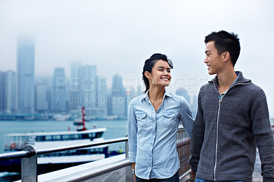 Buy stock photo Shot of a young asian couple walking along the Hong Kong waterfront