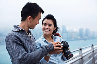 Buy stock photo Shot of a young couple looking at photos on a digital slr in front of the Hong Kong skyline