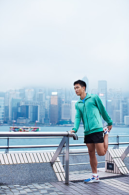 Buy stock photo Shot of a young asian man warming up for a jog along the Hong Kong skyline