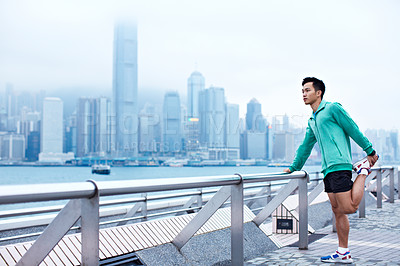 Buy stock photo Shot of a young asian man warming up for a jog along the Hong Kong skyline