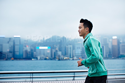 Buy stock photo Shot of a young man jogging along the Hong Kong waterfront