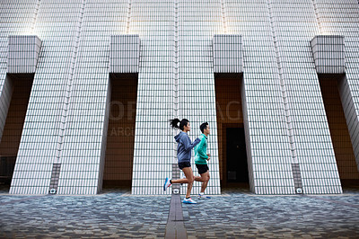 Buy stock photo Full length shot of a young man and woman jogging in front of a building's facade