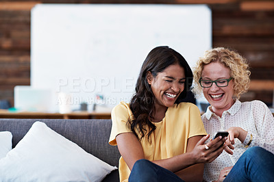 Buy stock photo Shot of two colleagues laughing together while looking at a cellphone