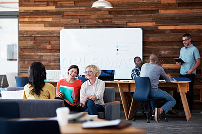 Buy stock photo Shot of three colleagues discussing paperwork in a modern office with colleagues blurred in the background