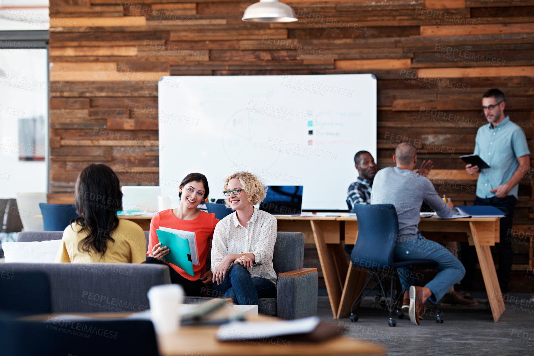 Buy stock photo Shot of three colleagues discussing paperwork in a modern office with colleagues blurred in the background