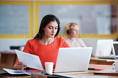 Buy stock photo Shot of a designer working at her desk with her colleague blurred in the background