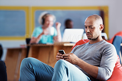 Buy stock photo Shot of a man texting at the office with his colleagues in the background