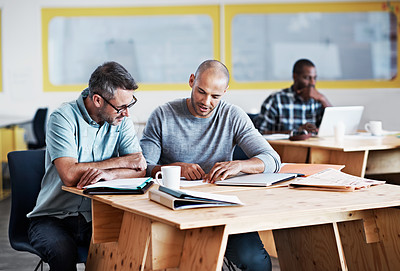 Buy stock photo Shot of two male coworkers discussing paperwork at a desk in an office
