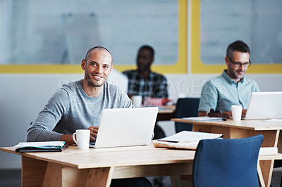 Buy stock photo Portrait of a man using his laptop with his colleagues blurred in the background