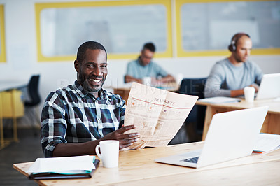 Buy stock photo Shot of a man reading a newspaper with his colleagues blurred in the background