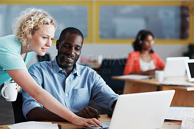 Buy stock photo Shot of a woman helping her coworker with his laptop with their colleague blurred in the background