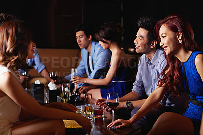 Buy stock photo Shot of a group of friends sitting in a nightclub enjoying drinks 