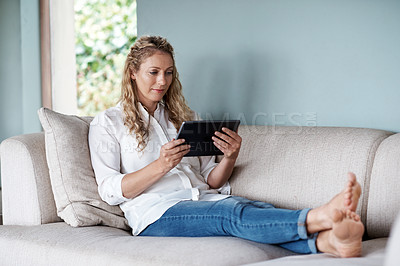Buy stock photo Full length shot of an attractive woman using a tablet while relaxing on the sofa