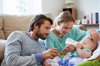 Buy stock photo Shot of a young couple feeding their baby at home