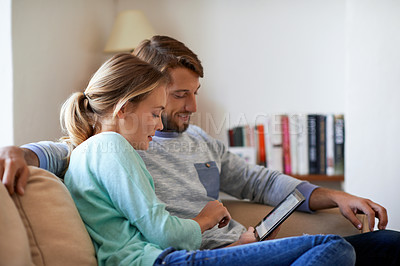Buy stock photo Shot of a young couple using a digital tablet while relaxing on a sofa at home