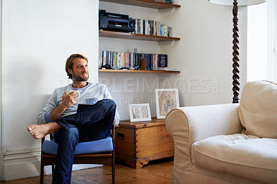 Buy stock photo Shot of a young man using a digital tablet and drinking a coffee while relaxing at home