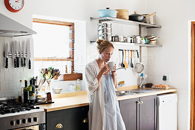 Buy stock photo Shot of a young woman drinking a coffee in the kitchen in the morning