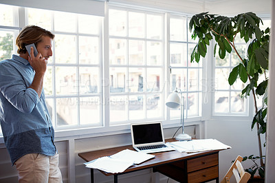 Buy stock photo Shot of a young man talking on his cellphone in his study at home