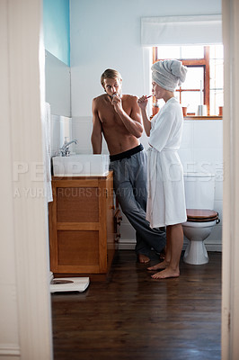 Buy stock photo Shot of a young couple brushing their teeth in the bathroom in the morning