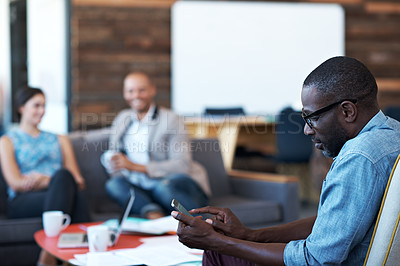 Buy stock photo Cropped shot of a businessman sending a text with his colleagues in the background