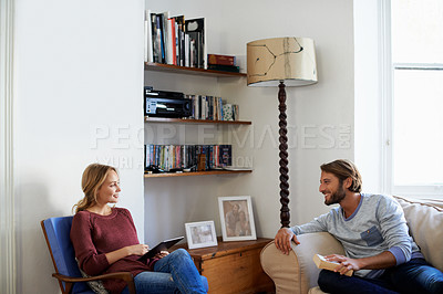 Buy stock photo Shot of a young couple relaxing with a book and digital tablet in their living room
