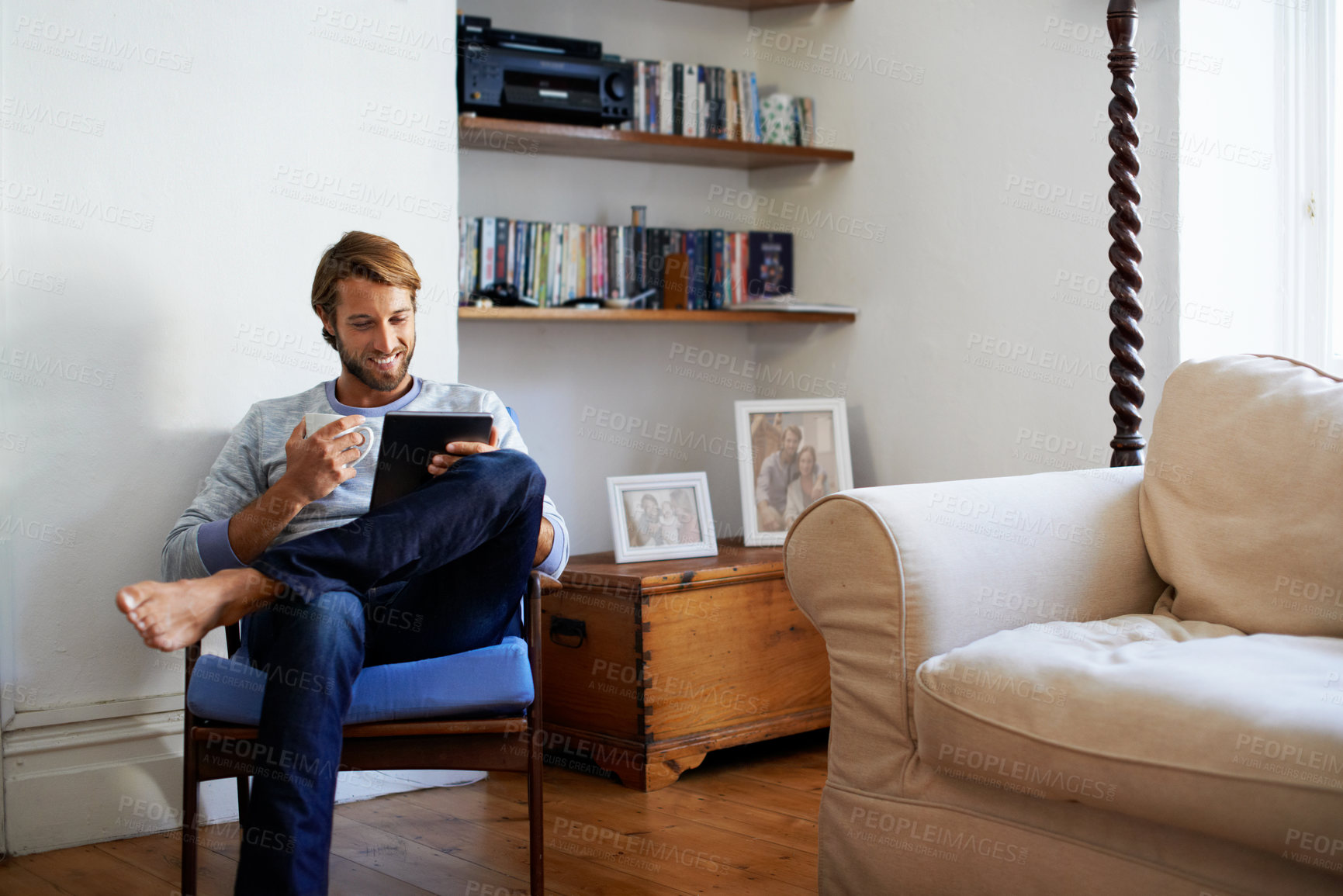Buy stock photo Shot of a young man having coffee while using his digital tablet at home