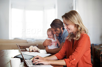 Buy stock photo Shot of a young woman using a laptop with her husband and baby sitting in the background