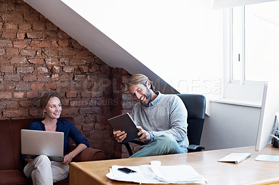 Buy stock photo Shot of a young couple using a digital tablet and laptop while relaxing at home
