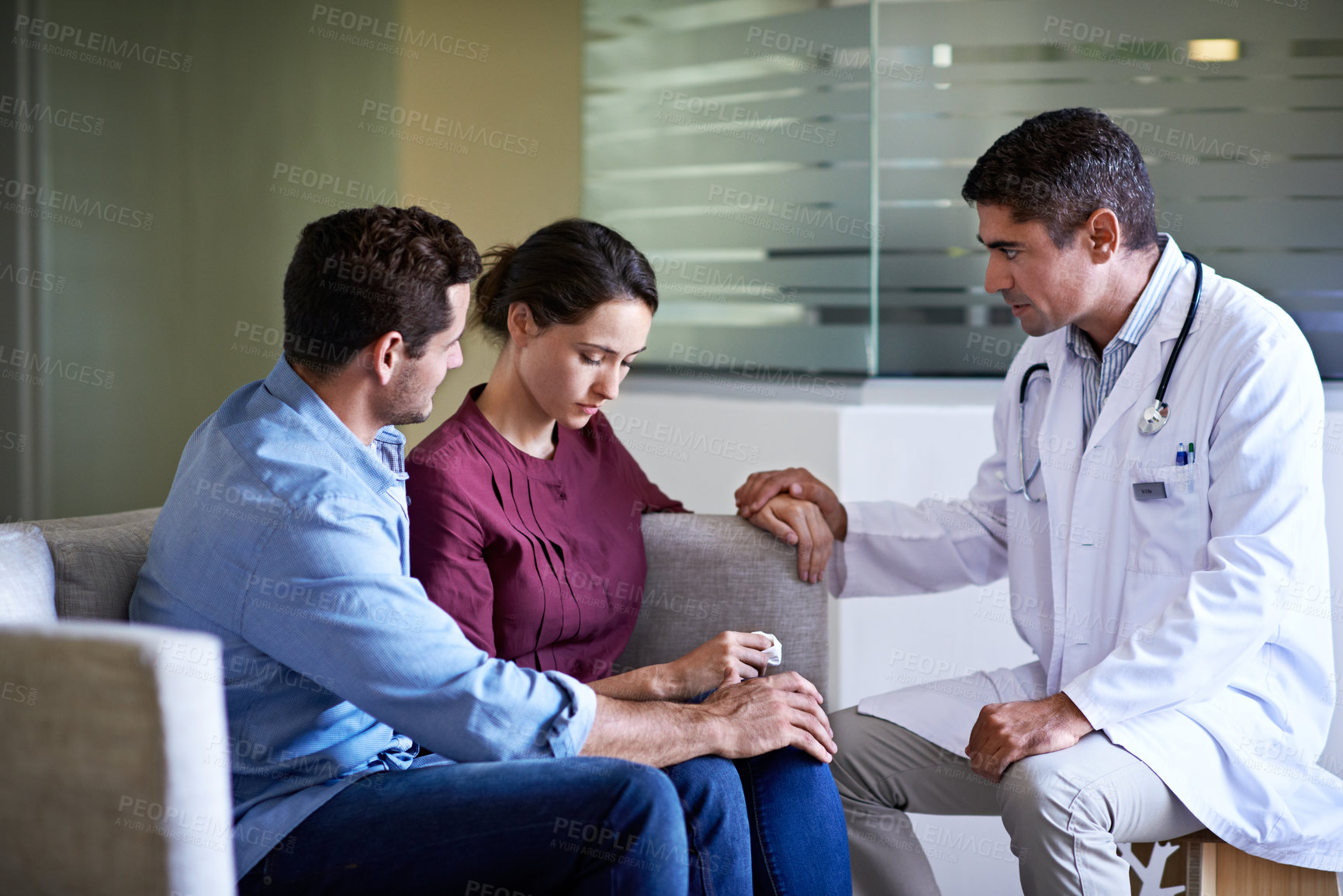 Buy stock photo Shot of a compassionate doctor delivering news to a couple in a hospital waiting room