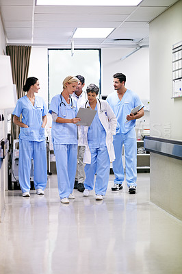 Buy stock photo Shot of a team of doctors walking and talking in a hospital corridor