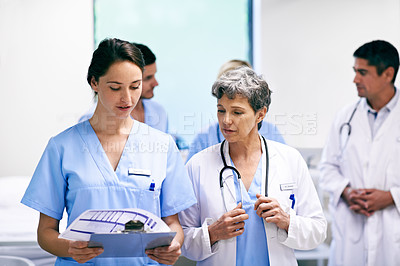 Buy stock photo Shot of a team of doctors walking and talking in a hospital corridor