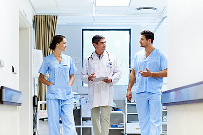 Buy stock photo Shot of a team of doctors walking and talking in a hospital corridor