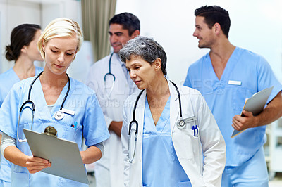 Buy stock photo Shot of a team of doctors walking and talking in a hospital corridor