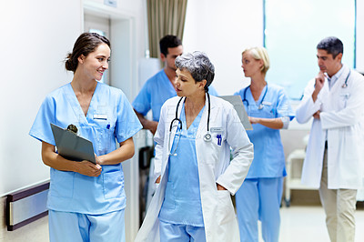 Buy stock photo Shot of a team of doctors walking and talking in a hospital corridor