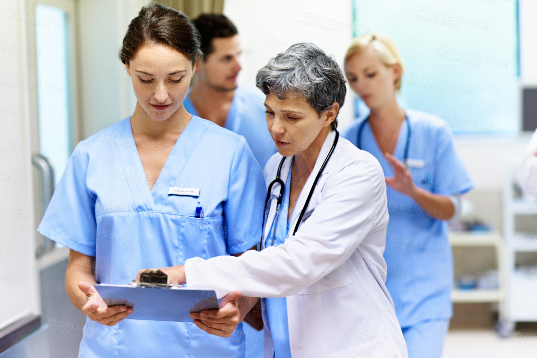 Buy stock photo Shot of a team of doctors walking and talking in a hospital corridor
