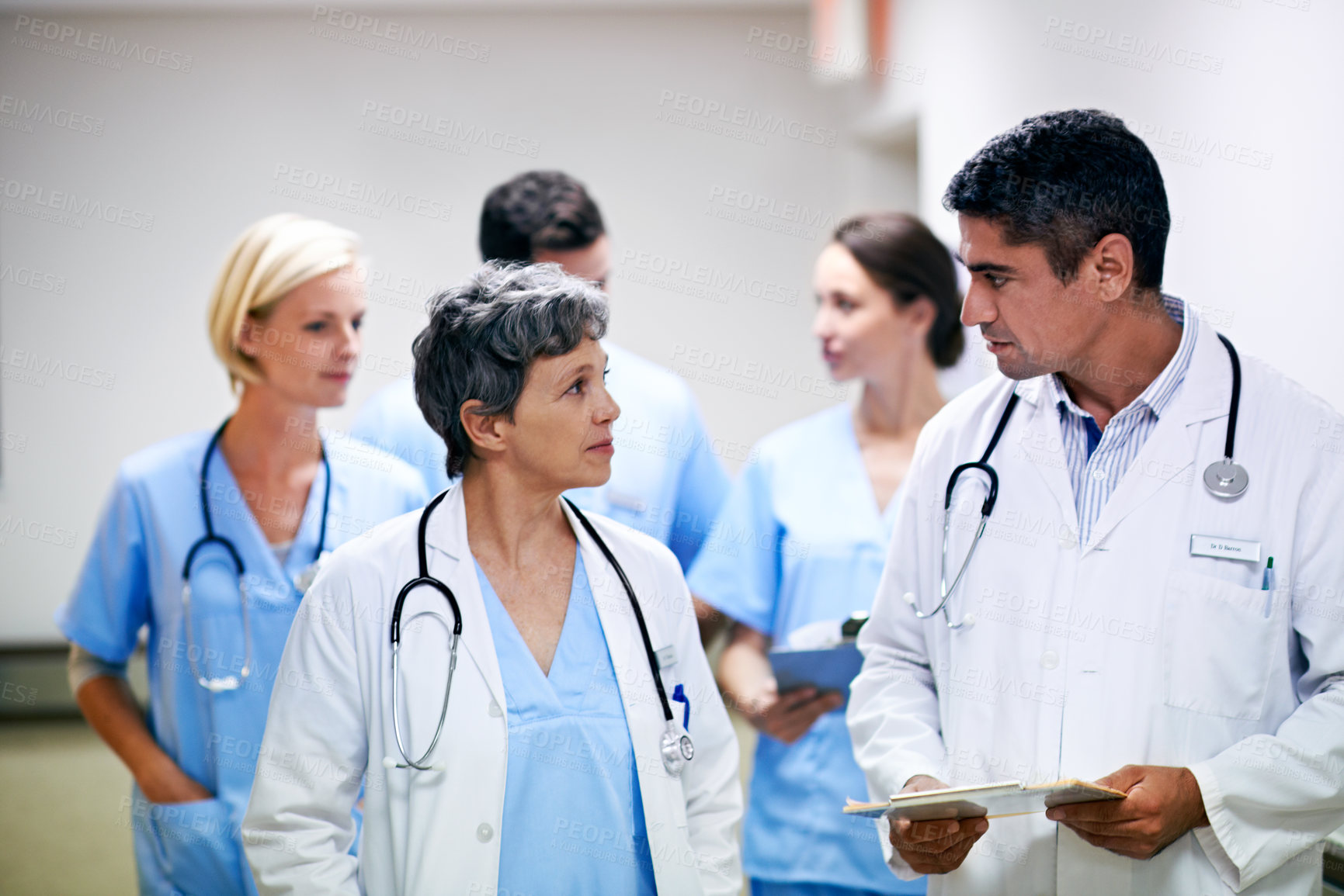 Buy stock photo Shot of a team of doctors walking and talking in a hospital corridor