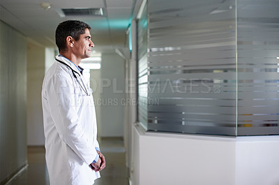 Buy stock photo Shot of a thoughtful-looking doctor standing in a hospital corridor