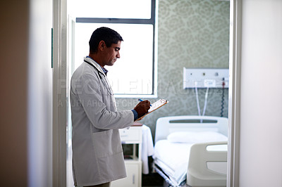 Buy stock photo Shot of a male doctor looking through paperwork while standing in a hospital ward