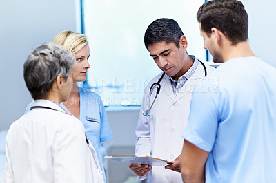 Buy stock photo Shot of a group of doctors looking through a medical report together while standing in a ward
