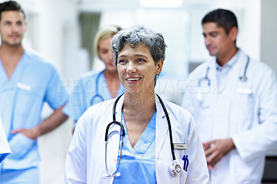 Buy stock photo Shot of a group of doctors walking down a hospital corridor