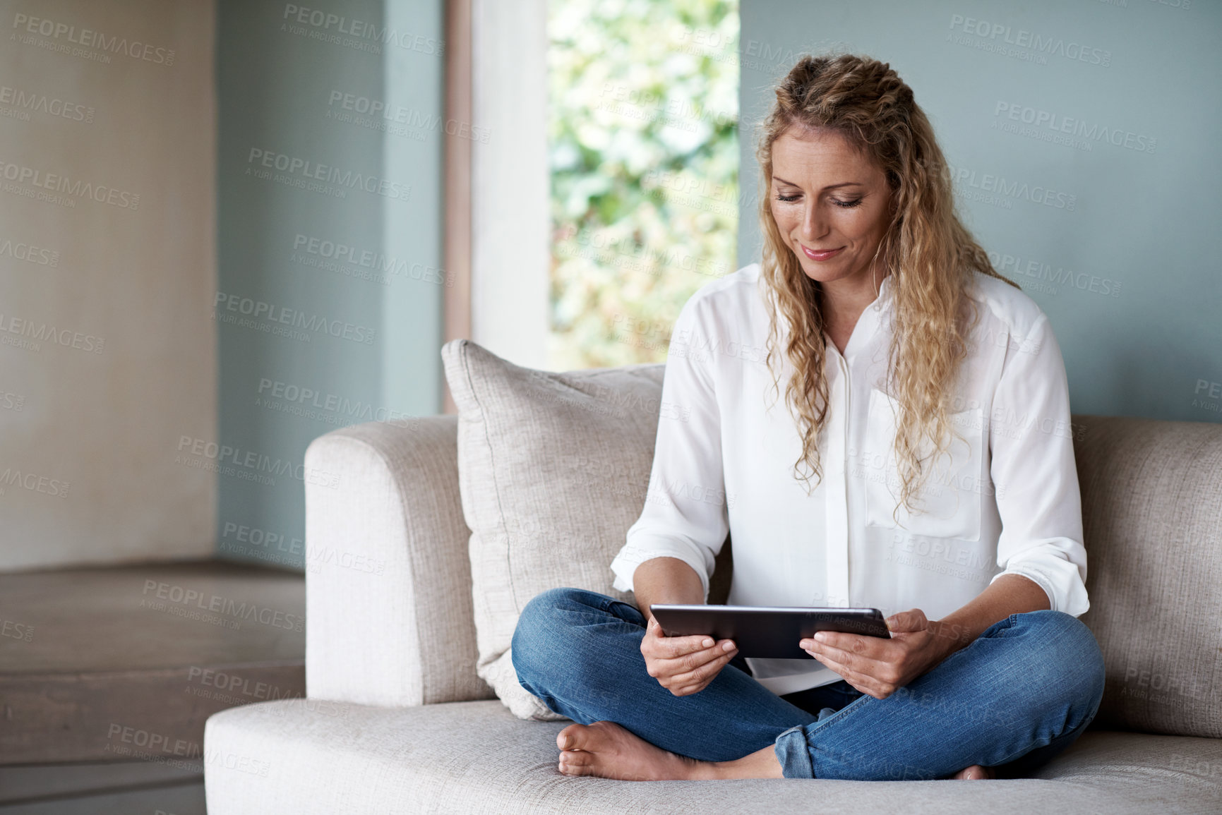 Buy stock photo Shot of a woman using her digital tablet while sitting in her living room