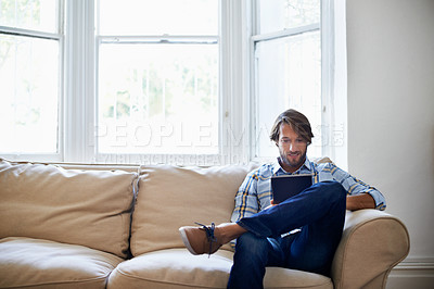 Buy stock photo Shot of a man using a digital tablet while relaxing at home
