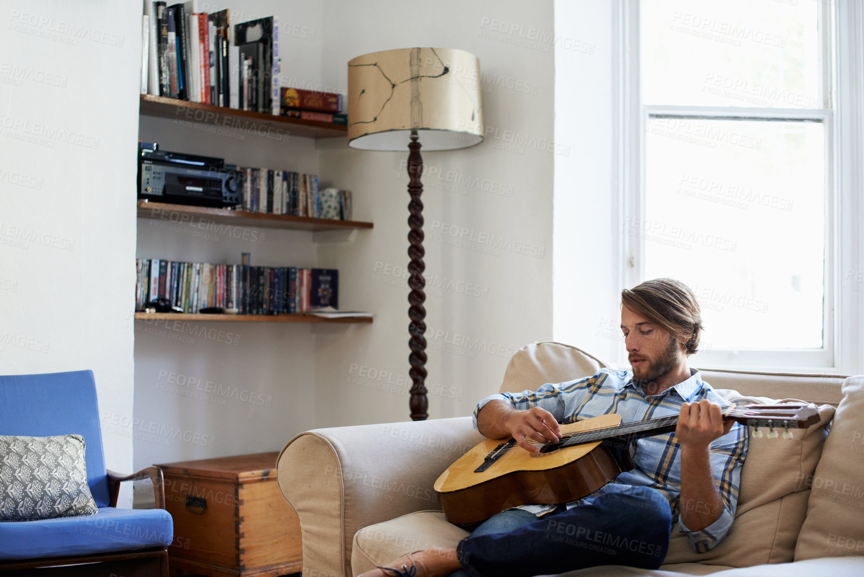 Buy stock photo Home, man and play guitar for music, practice song and talent performance on weekend. Sofa, person and musician with acoustic instrument for creative hobby, audio and strum with rhythm at apartment